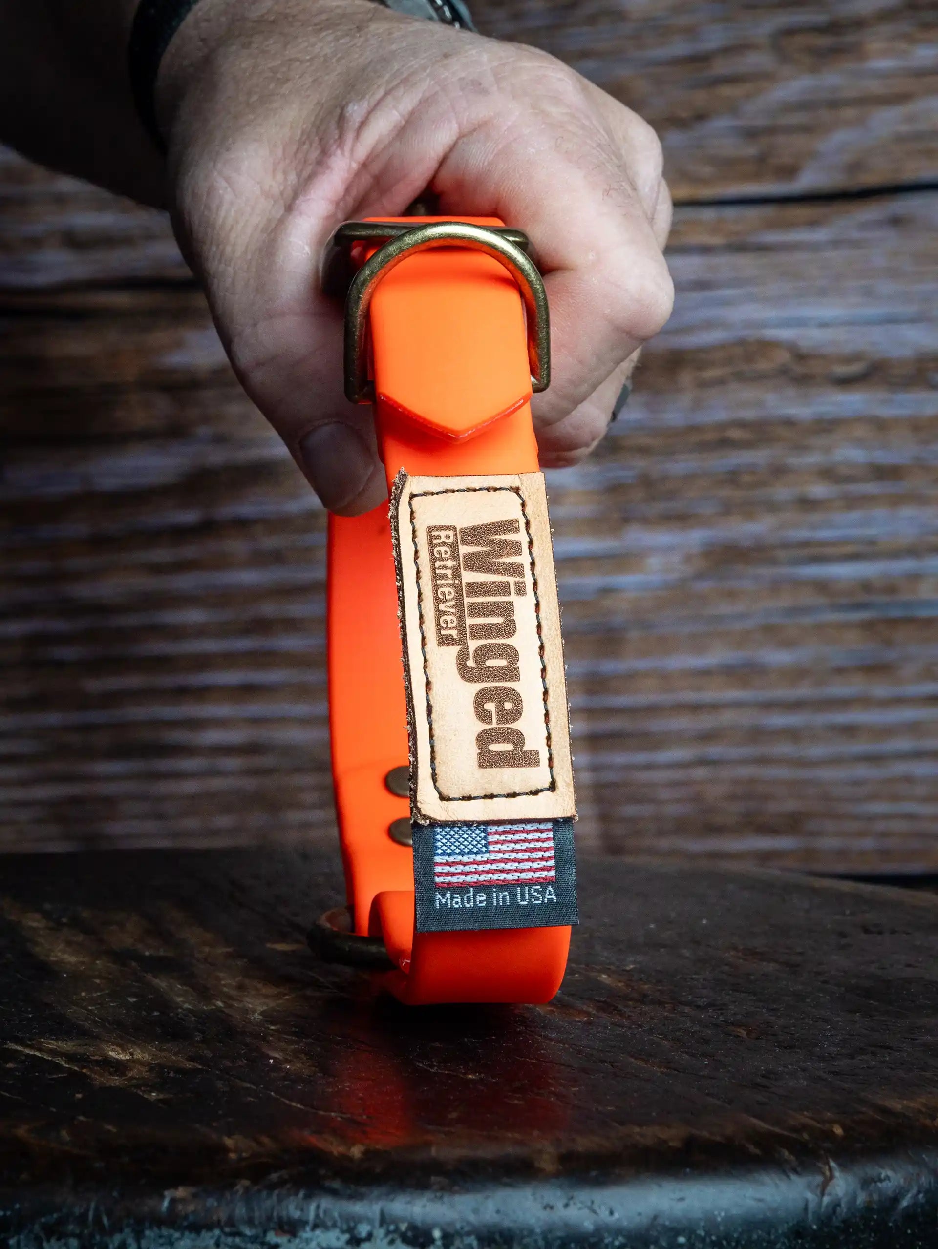 Patternmaster Jenny's Will Collar in orange with brass buckle, held by a hand.